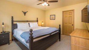 Une chambre à coucher comprenant un lit, des tables de chevet, un ventilateur de plafond, une porte et une commode.