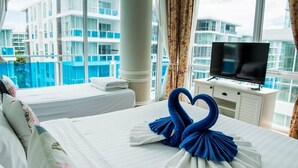 A hotel room with a bed, a TV, and a view of a building with balconies. - D606 Bright 2-bedroom apartment with Playground near Sea, city (Huahin)