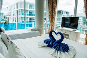 Ett hotellrum med en säng, en tv och utsikt över en byggnad med balkonger.
