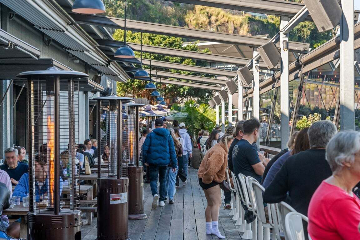 Un espace extérieur aménagé pour les repas, avec des tables et des chaises, entouré d’une allée couverte agrémentée de guirlandes lumineuses.