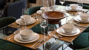 A dining table set with white plates, bowls, and cutlery, surrounded by green upholstered chairs. - Thoughtfully Designed Del Ray Xcape (Alexandria)