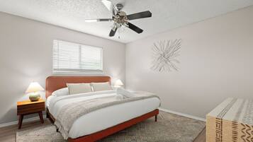 A bedroom with a bed, two bedside lamps, a ceiling fan, a window with blinds, a patterned rug, and a decorative wall piece.
