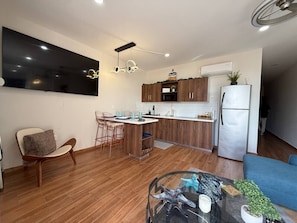 Eine moderne Küche mit Holzschränken, einer eingebauten Mikrowelle und einem Kühlschrank. Es gibt einen Essbereich mit einem Glastisch und Stühlen.