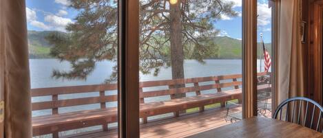 Um deck de madeira com mesa e cadeiras, com vista para um lago com uma árvore e um banco.