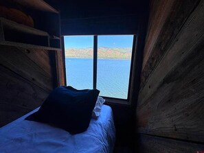 A cabin with a bed and a window overlooking a body of water. - Vallecito Lakefront Cabin (Bayfield)