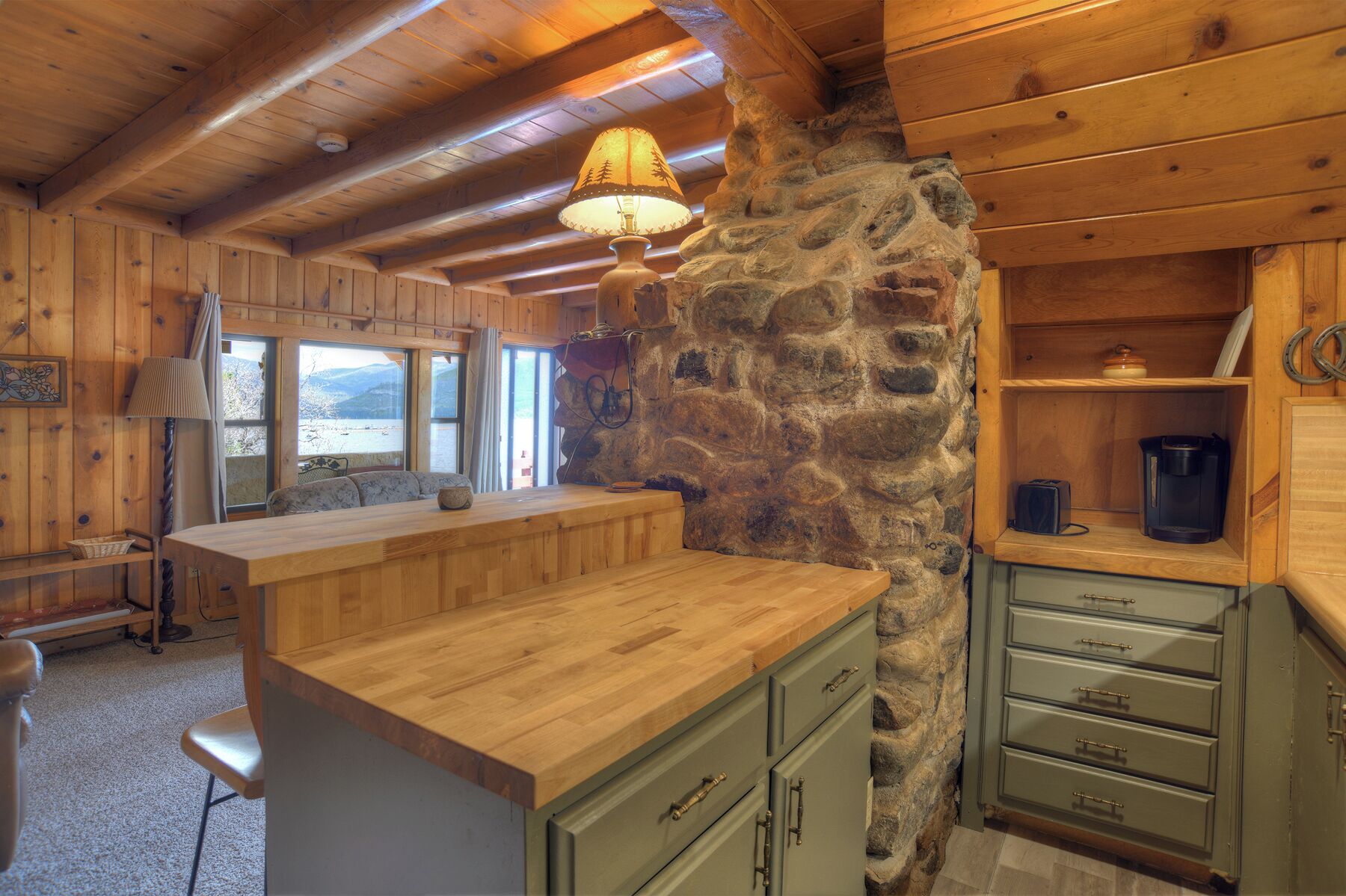 A rustic cabin interior with a stone wall, wooden furniture, and a view through a window.