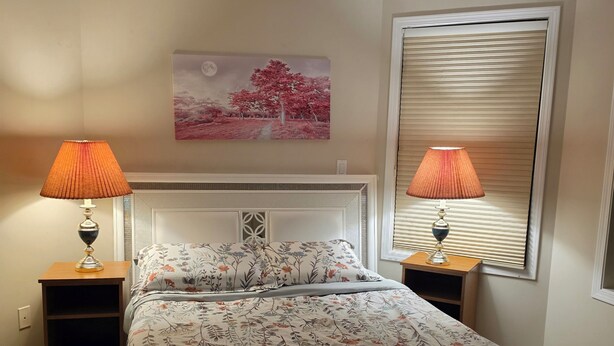 A bedroom with a bed, two bedside lamps, a nightstand, a wall-mounted painting, and a window with blinds. - Gamma
A beautiful master bedroom with bathroom in a town house. (Fort McMurray)