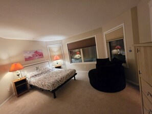 Ein Schlafzimmer mit einem Bett, Nachttischlampen, einem Sessel und einem Kleiderschrank.