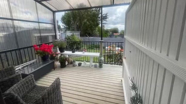 A covered outdoor area with a wooden deck, wicker furniture, and potted plants.