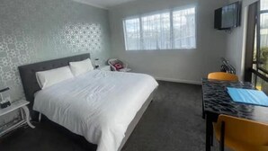 A hotel room with a bed, a desk, a chair, a television, and a window. - Mitchell's Bay BnB (Riverton / Aparima)