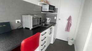 A compact kitchen with a red bar stool, white cabinets, a microwave, and a coffee maker. - Mitchell's Bay BnB (Riverton / Aparima)