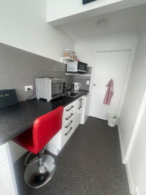 A compact kitchen with a red bar stool, white cabinets, a microwave, and a coffee maker.