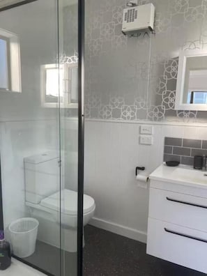 A bathroom with a toilet, a glass shower enclosure, a white sink, and a microwave on the countertop.