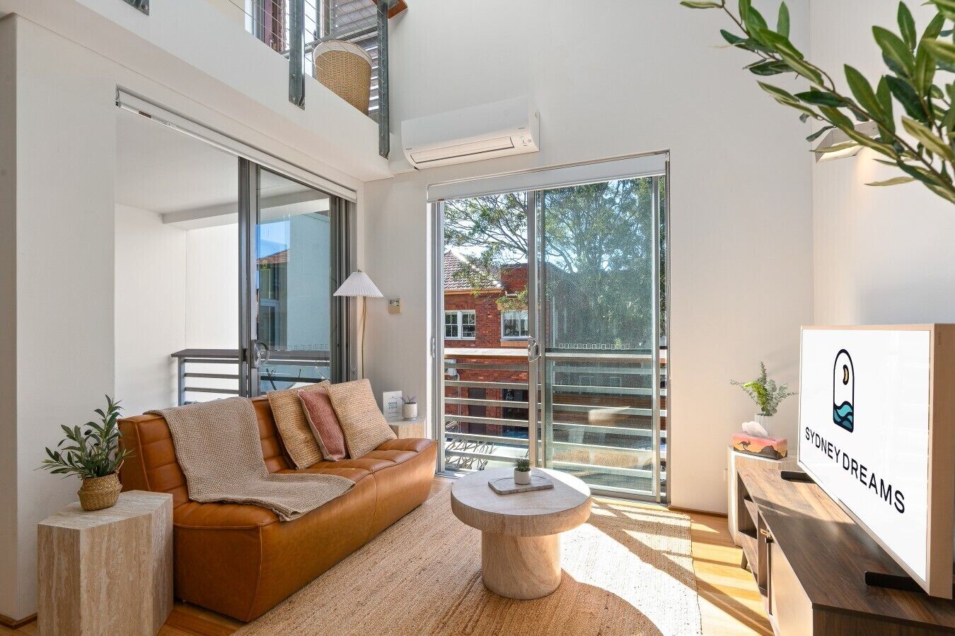 Uma sala de estar moderna com um sofá de couro, uma mesa de centro redonda e uma grande janela com vista para um edifício de tijolos.