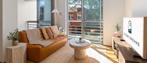 Uma sala de estar moderna com um sofá de couro, uma mesa de centro redonda e uma grande janela com vista para um edifício de tijolos.