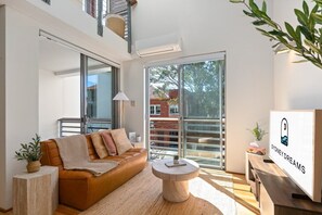 A modern living room with a leather sofa, a round coffee table, and a large window with a view of a brick building. - Sunny Balcony, Luxury in the Heart Of Bondi Beach (Bondi Beach)