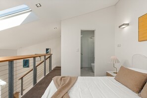A modern bedroom with a bed, a nightstand, a lamp, a wooden headboard, a painting, a staircase, and a shower area. - Sunny Balcony, Luxury in the Heart Of Bondi Beach (Bondi Beach)