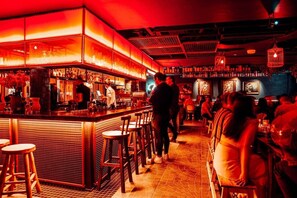 Eine Bar mit Hockern und Tischen, einem Barkeeper und Gästen.