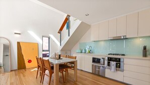 A modern kitchen with a dining area, featuring a wooden dining table, chairs, a built-in oven, and a microwave. - Sunny Balcony, Luxury in the Heart Of Bondi Beach (Bondi Beach)
