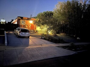 Un edificio residenziale con vialetto, un'auto parcheggiata e una casa con illuminazione esterna.