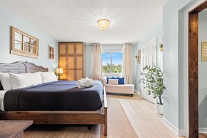 Ein Schlafzimmer mit einem Bett, einem Nachttisch, einem Fenster mit Vorhängen, einem Holzschrank und einer Topfpflanze.