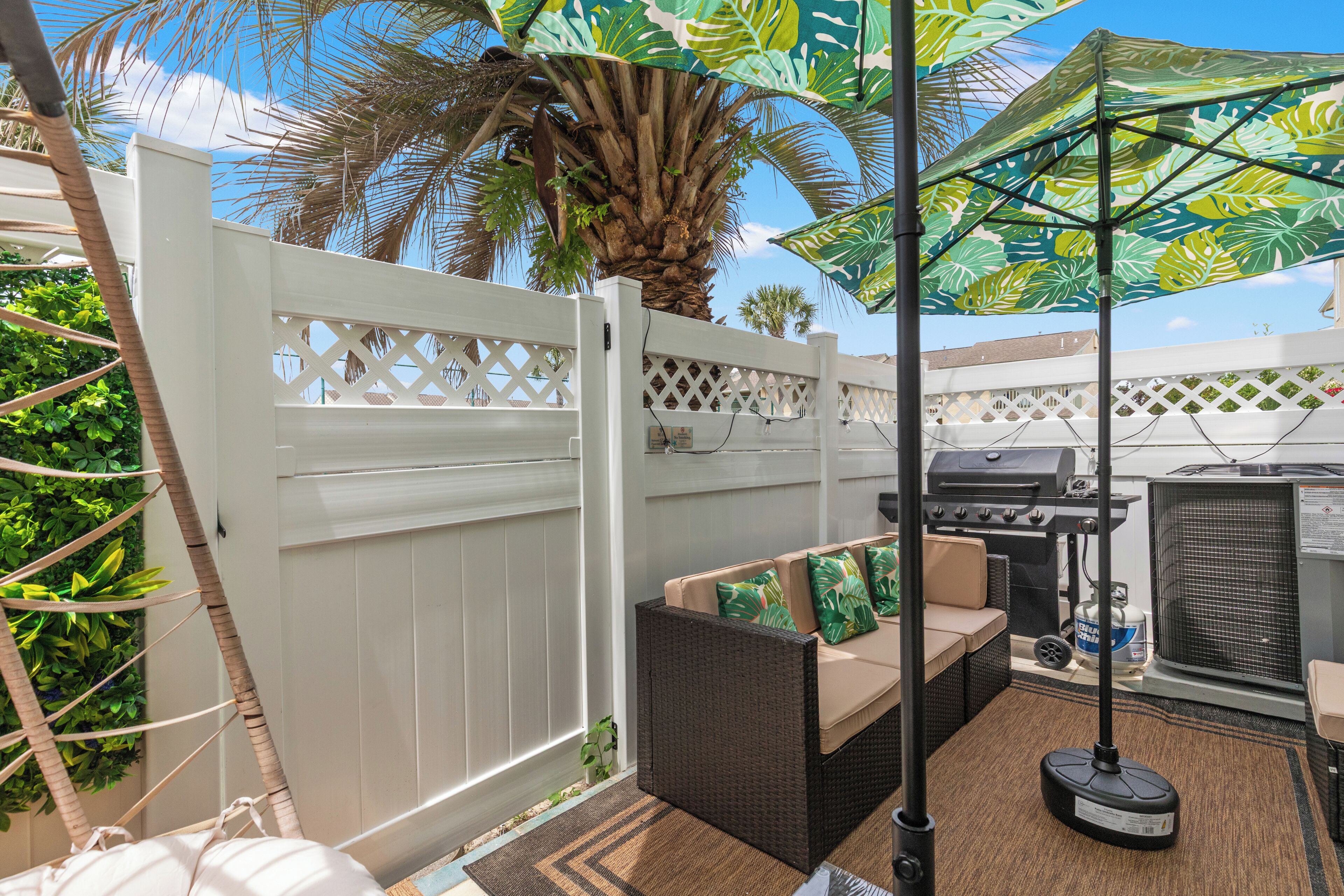 Une terrasse extérieure avec un barbecue, un espace salon et une clôture blanche.
