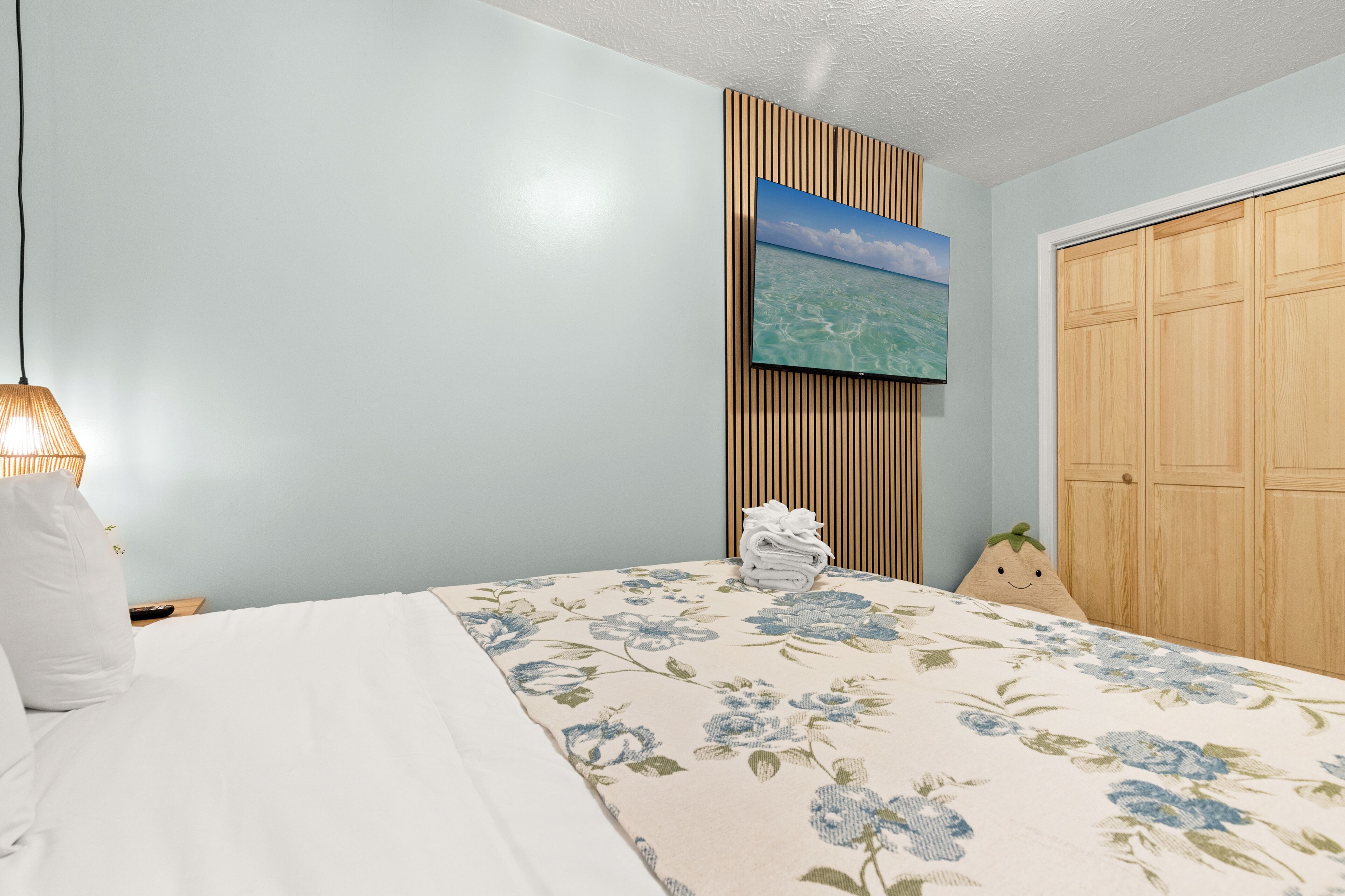 A bedroom with a bed, a wall-mounted TV, a wooden wardrobe, and a pillow with a smiley face.