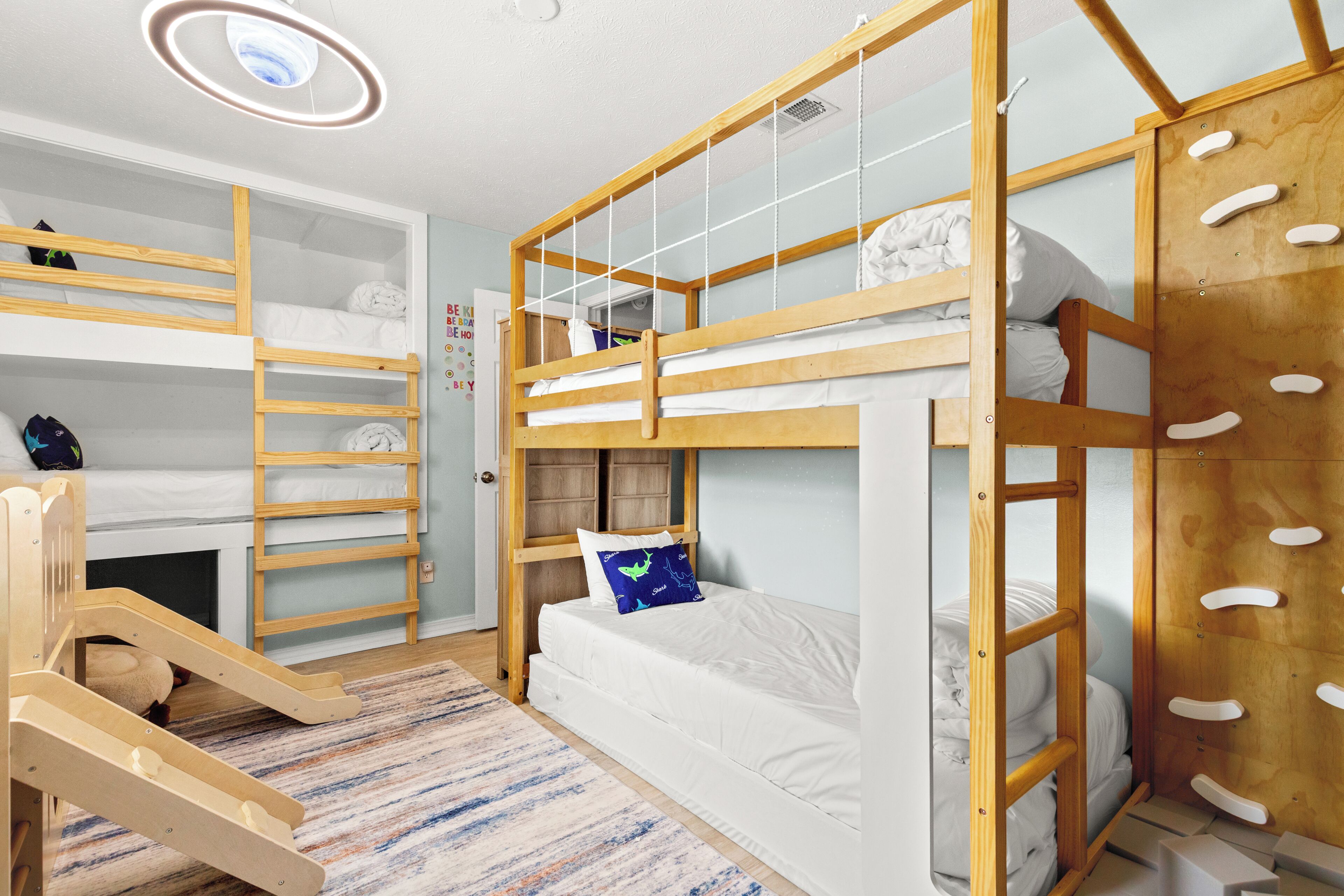 A bunk bed room with a wooden ladder, a small desk, and a patterned rug.