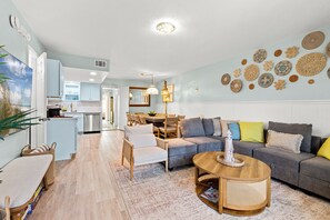 A modern living room with a grey sofa, a wooden coffee table, and a dining area with a white table and chairs. - Spacious PCB Resort Townhome with Golf Cart, 2 Kings, kids Room and Beach Access (Panama City Beach)