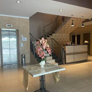 Un vestíbulo de hotel con una recepción, una escalera y un ascensor.