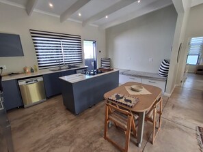 Cozinha moderna com ilha central, máquina de lavar louça embutida e área de refeições com mesa e cadeiras de madeira.