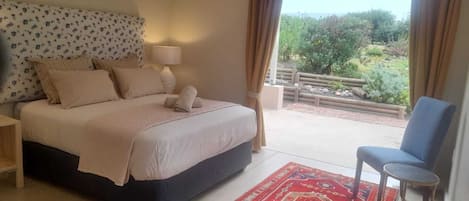 A bedroom with a bed, a nightstand, a lamp, a chair, and a view of the outdoors.