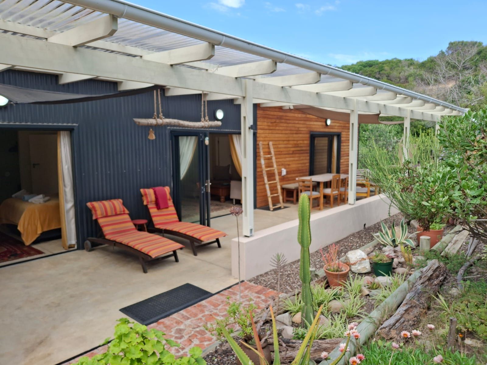 A modern outdoor seating area with a covered patio, a wooden interior, and a variety of desert plants.