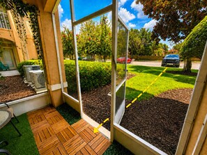 A patio area with a wooden deck, a glass door leading outside, and a view of a green lawn and parked cars. - 3 BR | Free water park | 5 min from Disney (Kissimmee)