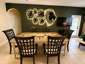 A dining area with a table, chairs, a decorative wall piece, and a television. - 3 BR | Free water park | 5 min from Disney (Kissimmee)