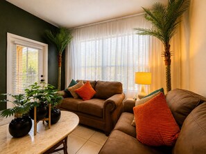 A living room with a brown sofa, a small table with a lamp, and potted plants. - 3 BR | Free water park | 5 min from Disney (Kissimmee)