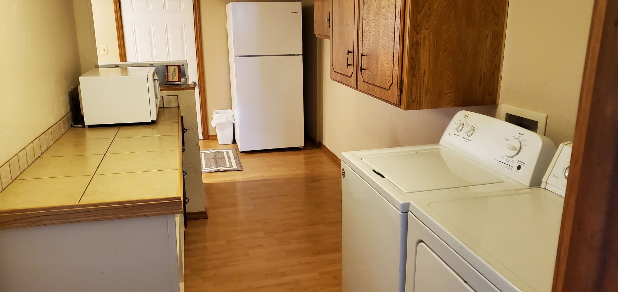 A compact kitchen with a washing machine, a refrigerator, and wooden cabinets.