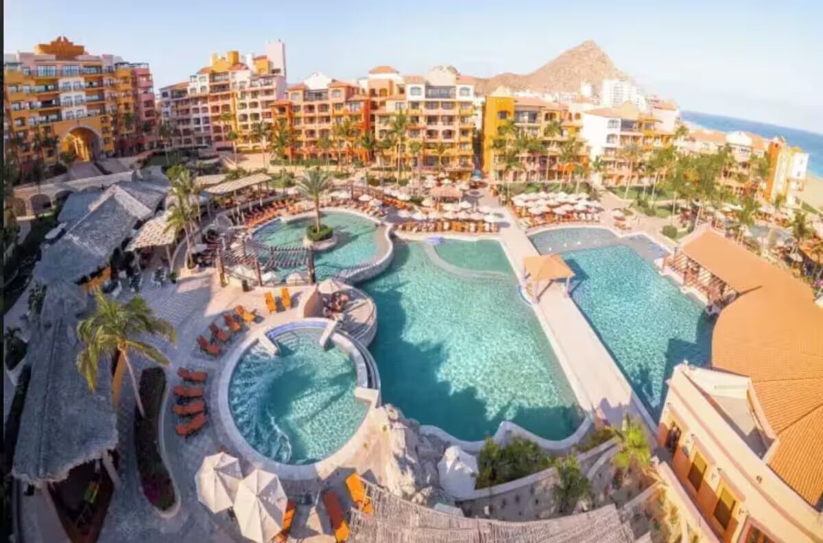 Ett semesterparadis med flera pooler, palmer och en imponerande bergskedja i bakgrunden.