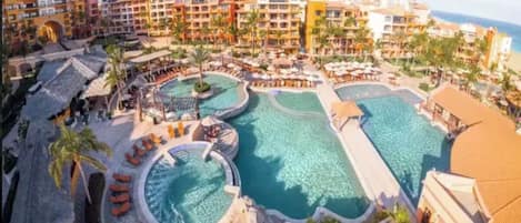 A resort with multiple swimming pools, palm trees, and a mountainous backdrop.
