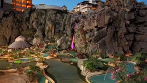 Ein Resort mit mehreren Schwimmbecken, einem Wasserfall und Gebäuden auf einer felsigen Klippe.