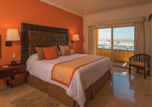 A hotel room with a large bed, a nightstand, a chair, and a view of the city through a balcony. -  Playa Grande Penthouse 2-Bedroom Suite on the Ridge Christmas & New Years weeks (Cabo San Lucas)