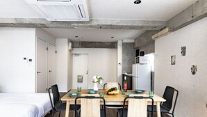 A compact room with a bed, a dining table with chairs, a kitchenette, and a door leading to another room. - AS7 Building (Sumida-ku)