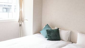 Ein Schlafzimmer mit Bett, Kissen, einem Fenster und Vorhängen.