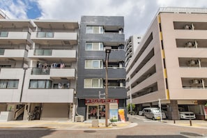 A multi-story residential building with balconies, a ground-level entrance, and a visible storefront with signage.