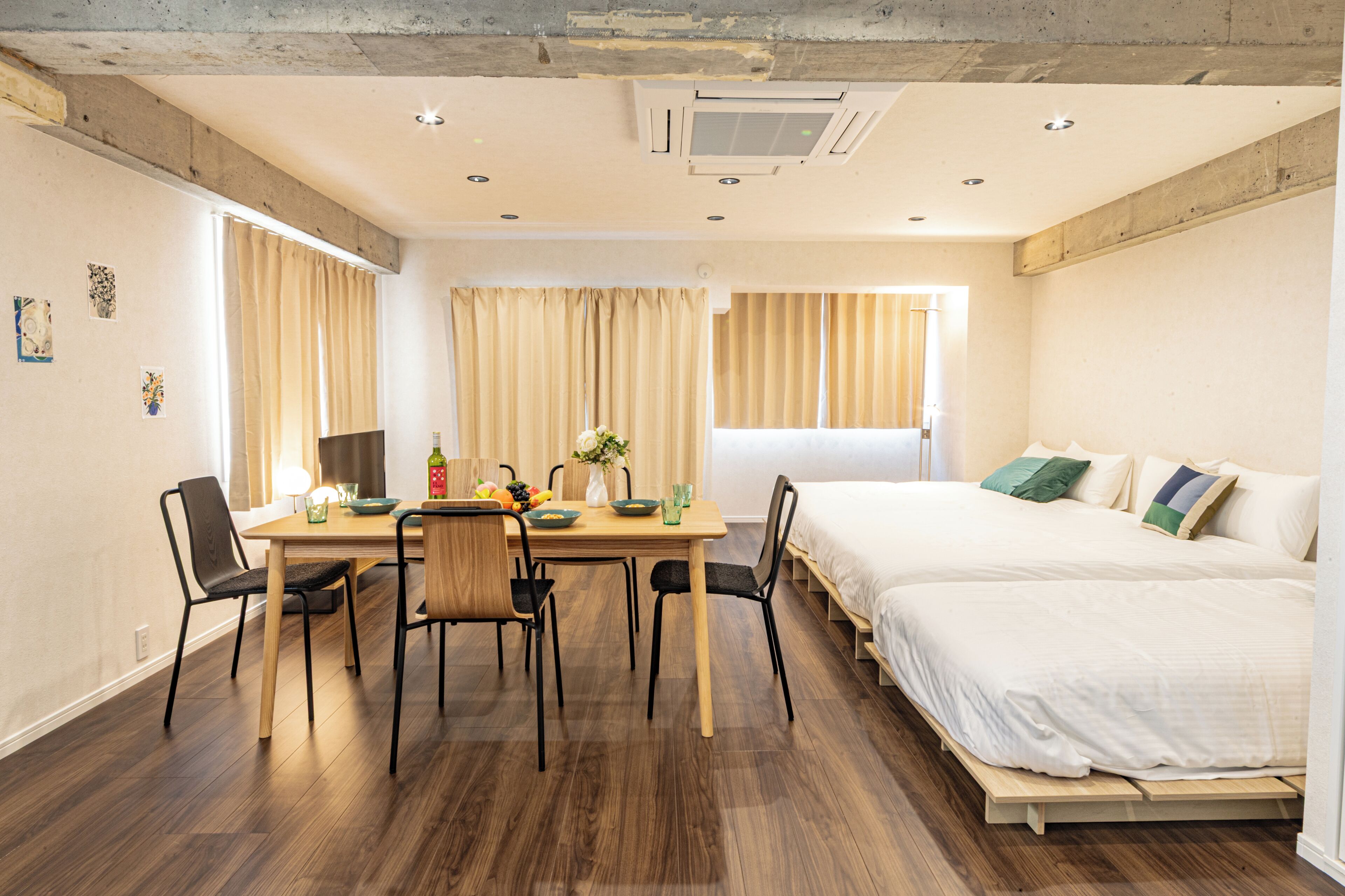 Una habitación moderna con una mesa de comedor de madera, sillas, una cama con ropa blanca y una ventana con cortinas.