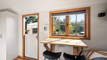 Une cuisine compacte avec une table en bois et deux chaises noires, une porte blanche et une fenêtre donnant sur des arbres.