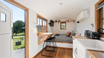 Une petite cuisine moderne et fonctionnelle, dotée d’un plan de travail en bois, d’un coin repas et d’un lit offrant une vue sur l’extérieur.