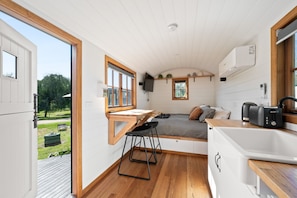 A compact, modern kitchenette with a wooden countertop, a small dining area, and a bed with a view of the outdoors. - Eldorado Caravan Park (Eldorado)