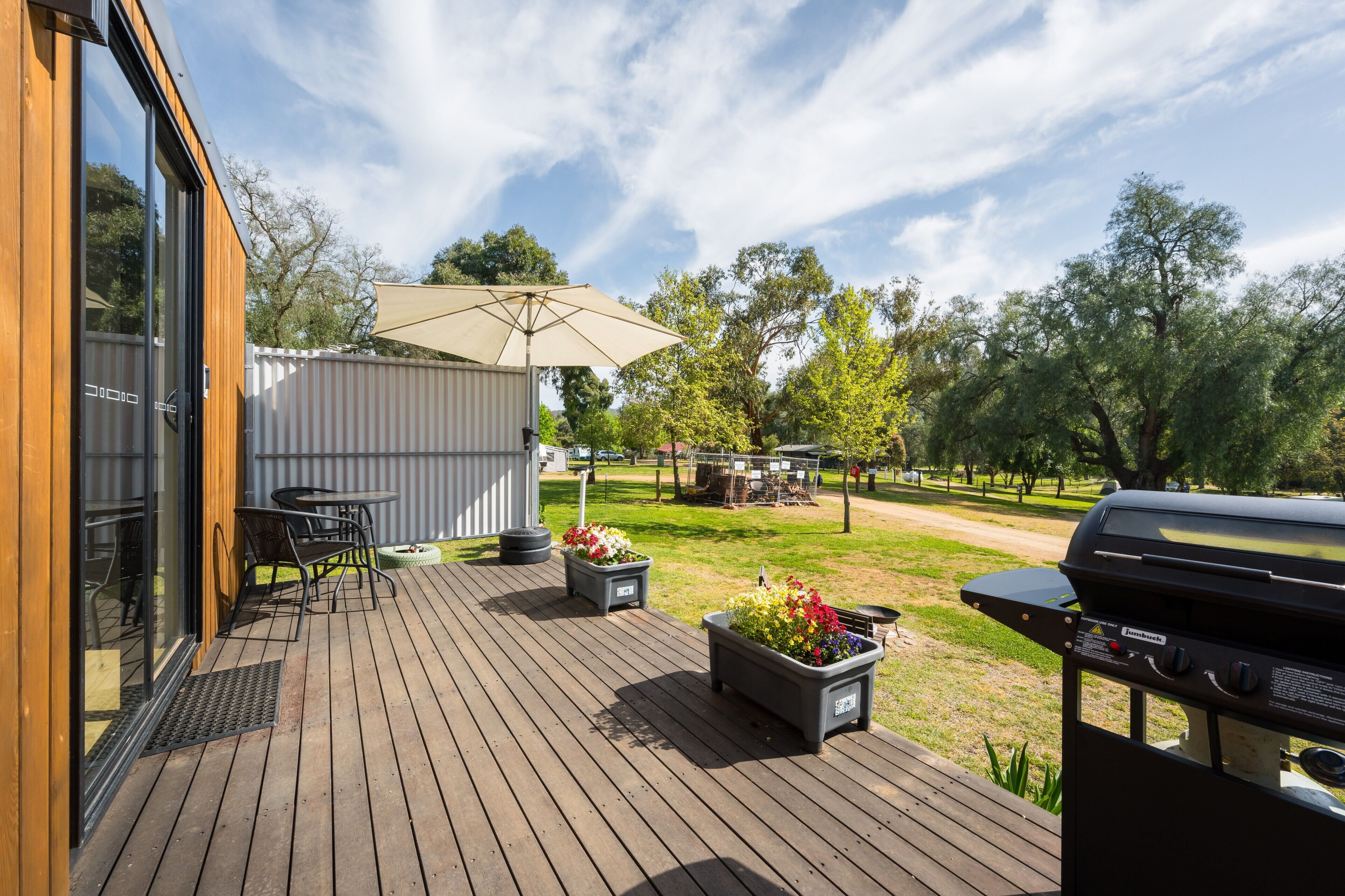An outdoor deck with a grill, a table with chairs, and a large umbrella.