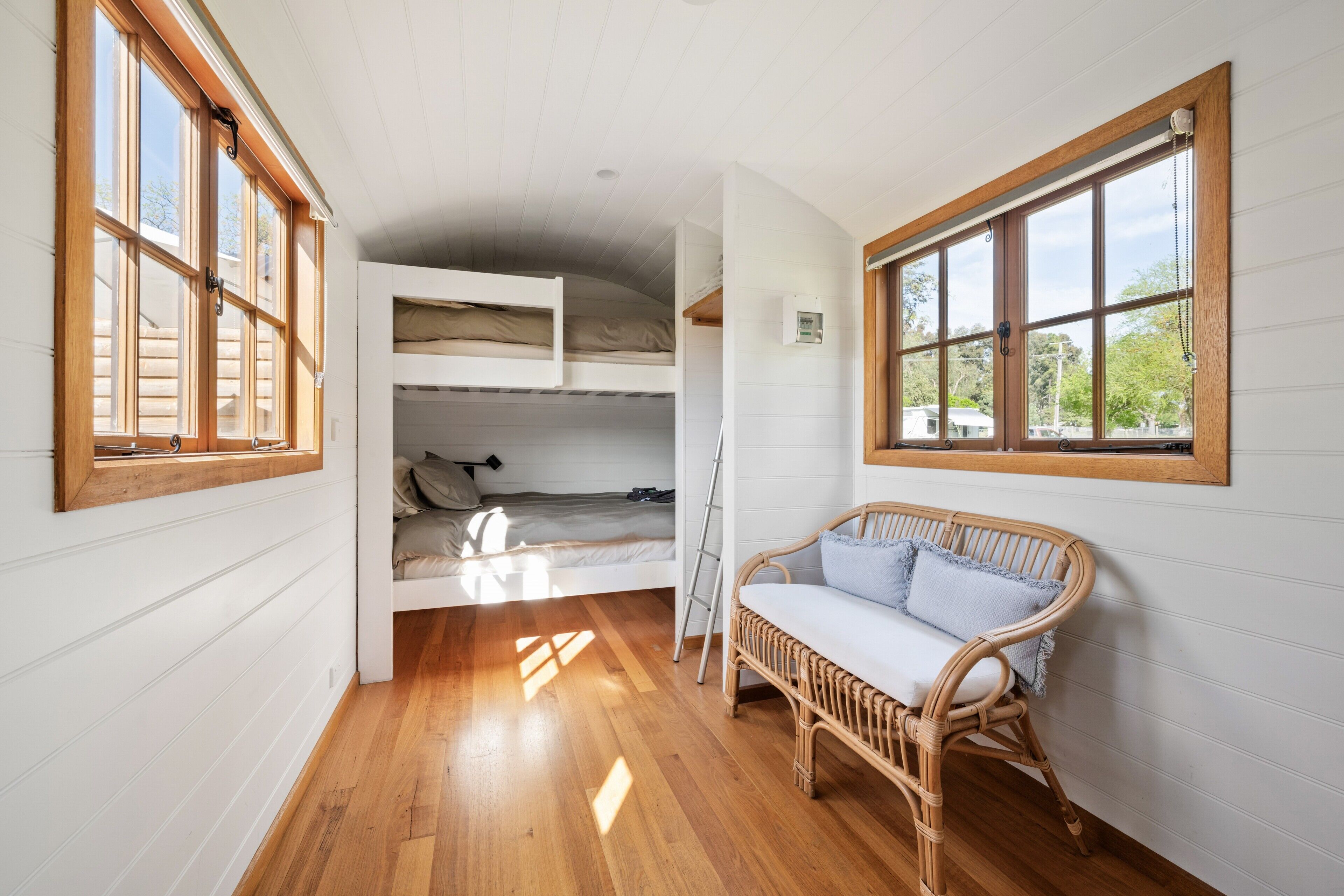 A room with a bunk bed, a wicker chair, and large windows.